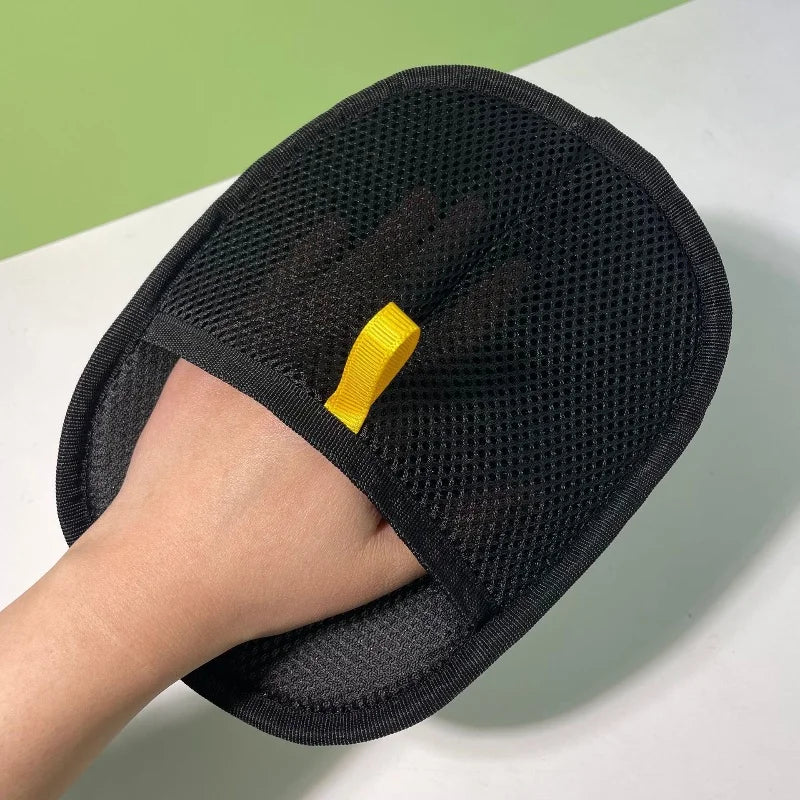 Black pet deshedding glove on a hand, textured mesh palm with yellow strap detail.