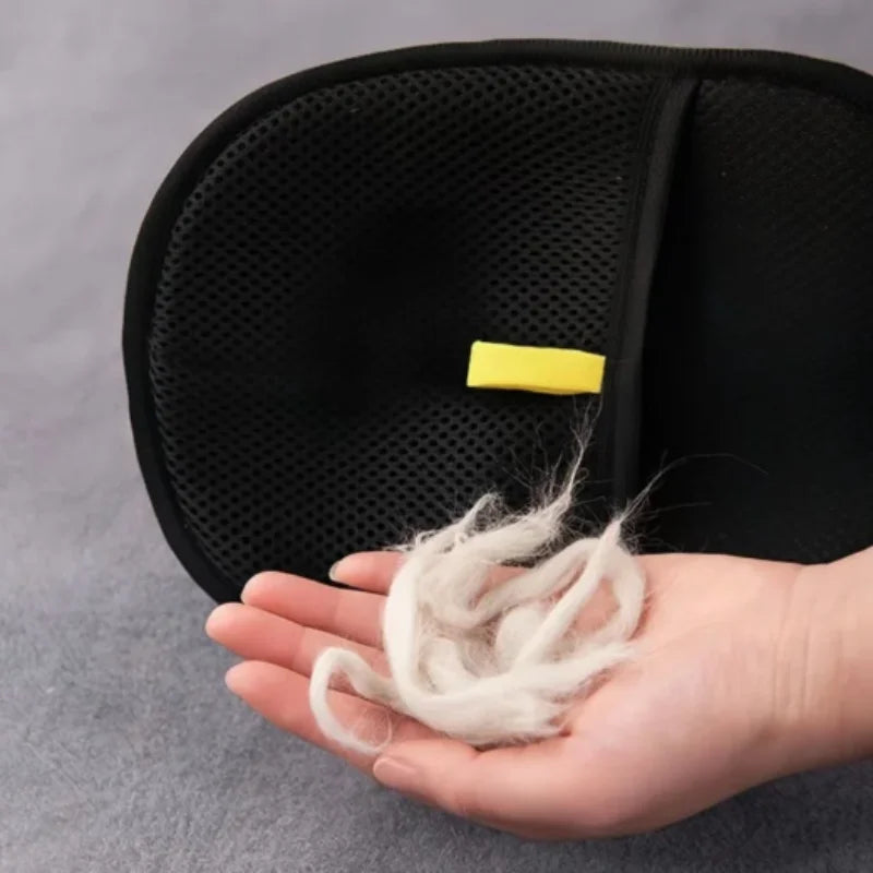 Black pet deshedding glove with mesh palm, featuring a yellow tab; hand holding it.